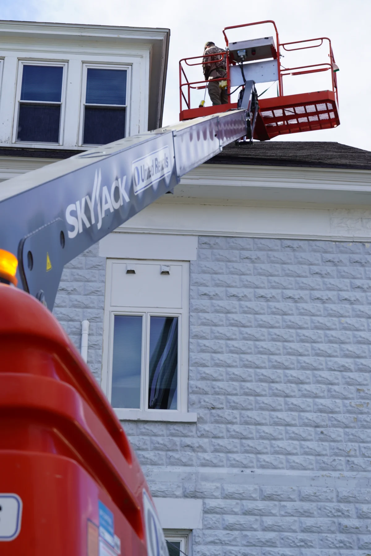Technician working from an aerial lift along the roofline of a white building